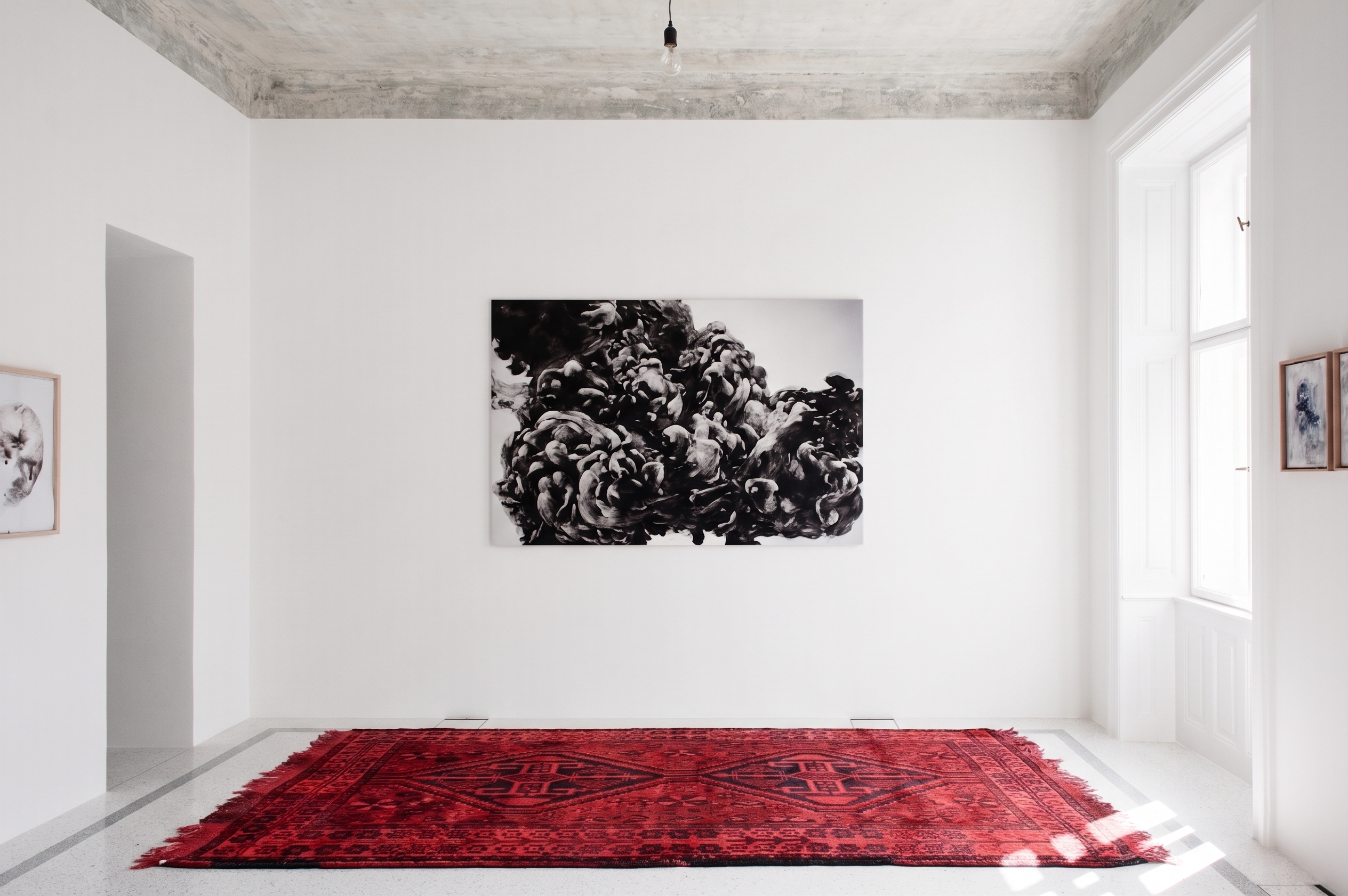 Heller Galerieraum mit abstraktem Schwarz-Weiß-Gemälde, hängender Pendelleuchte und einem großen dunkelroten Orientteppich mit geometrischem Muster